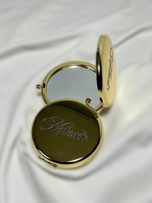 Gold compact mirror with 'Kallora Beauty' branding on a white fabric background